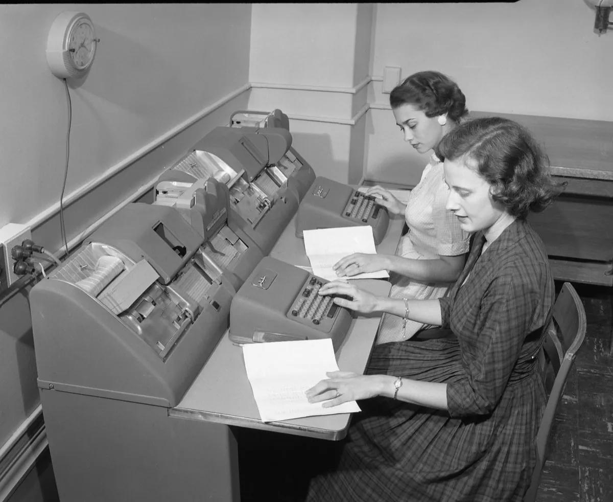 Two women in the 1950s working at keypunch machines, turning paper forms into punched cards one field at a time.