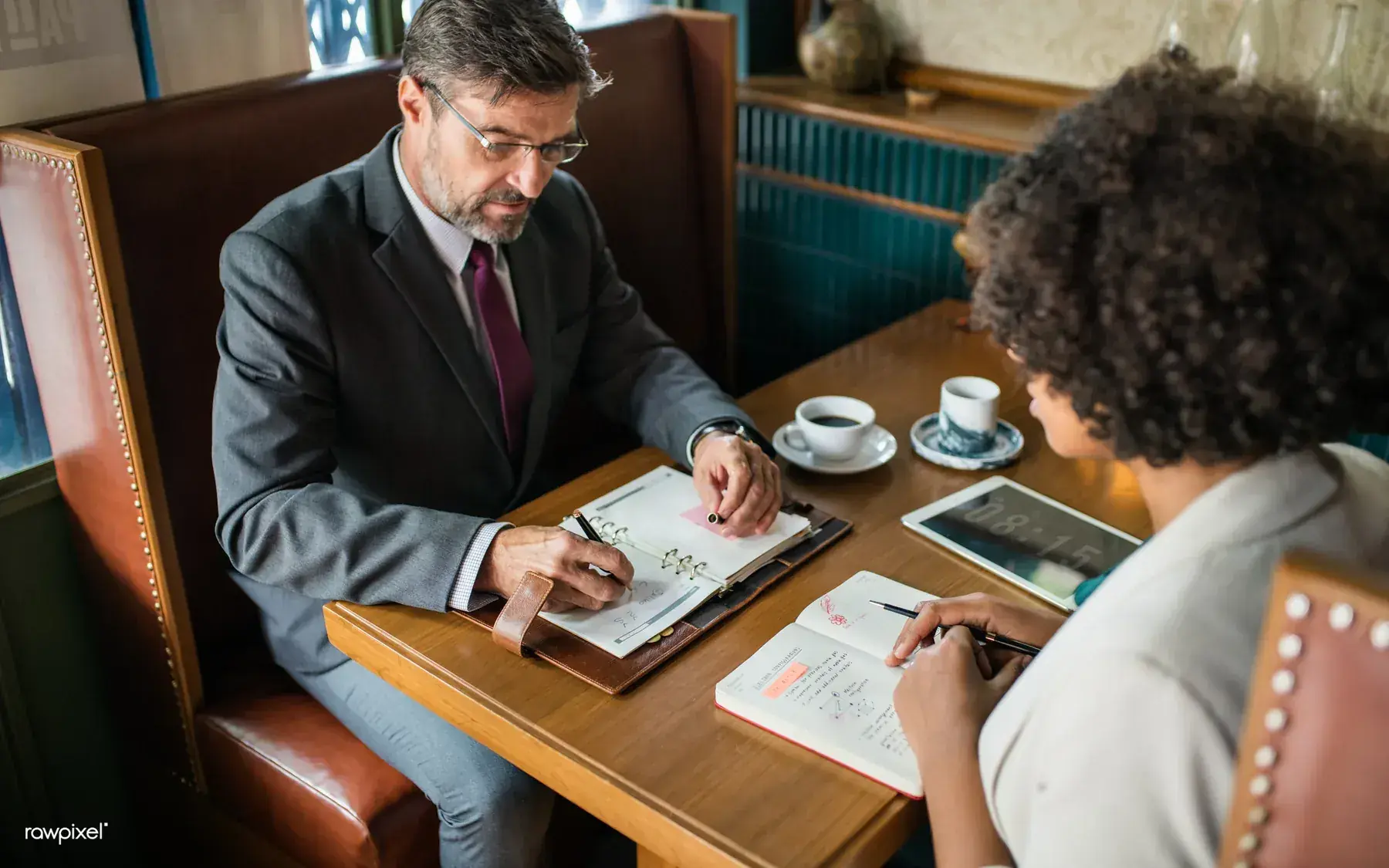 A small group of businesspeople talking and looking at a laptop together around a cafe table.