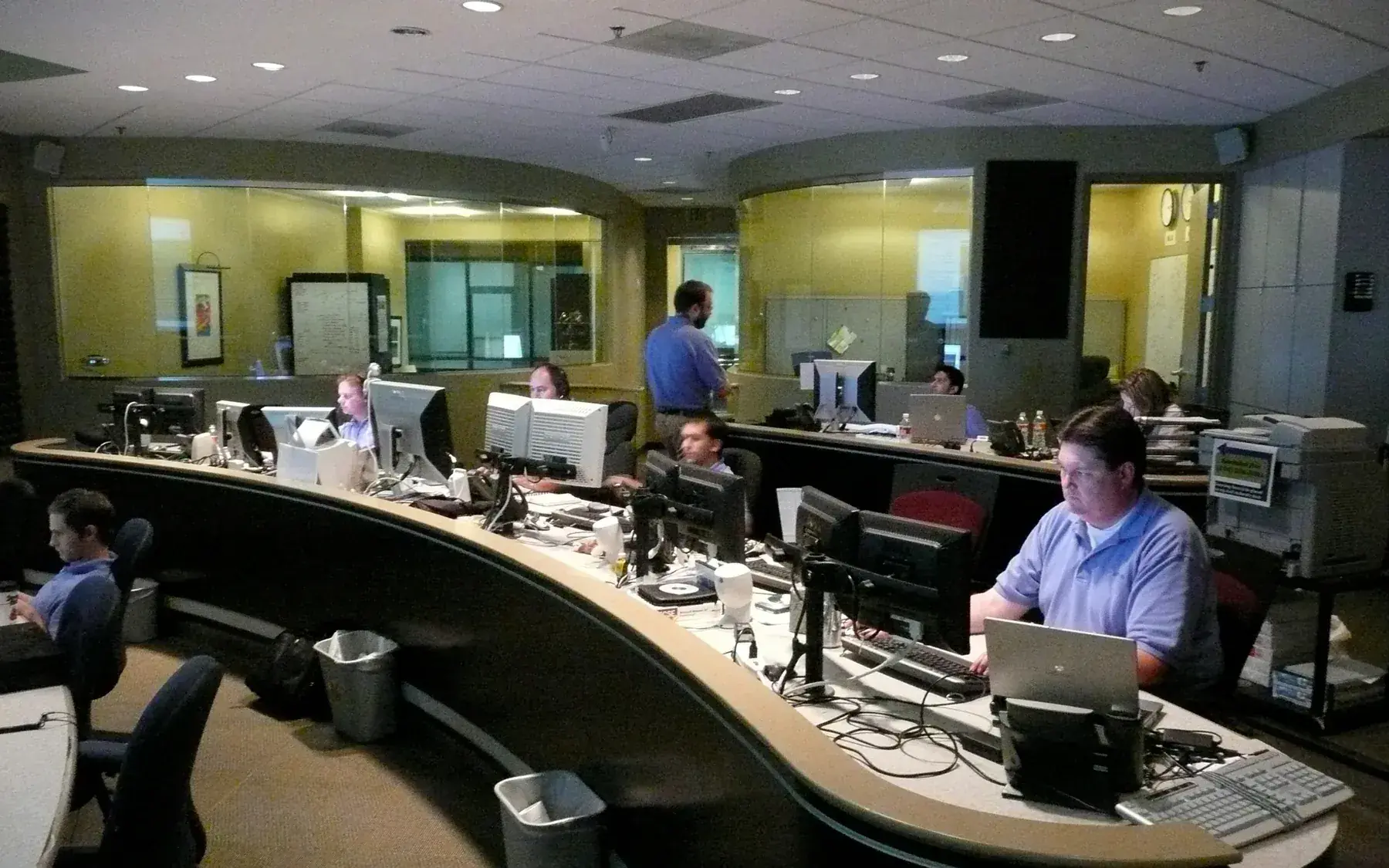 Technicians seated at a bank of multiple computer monitors displaying dense data inside a network operations center.