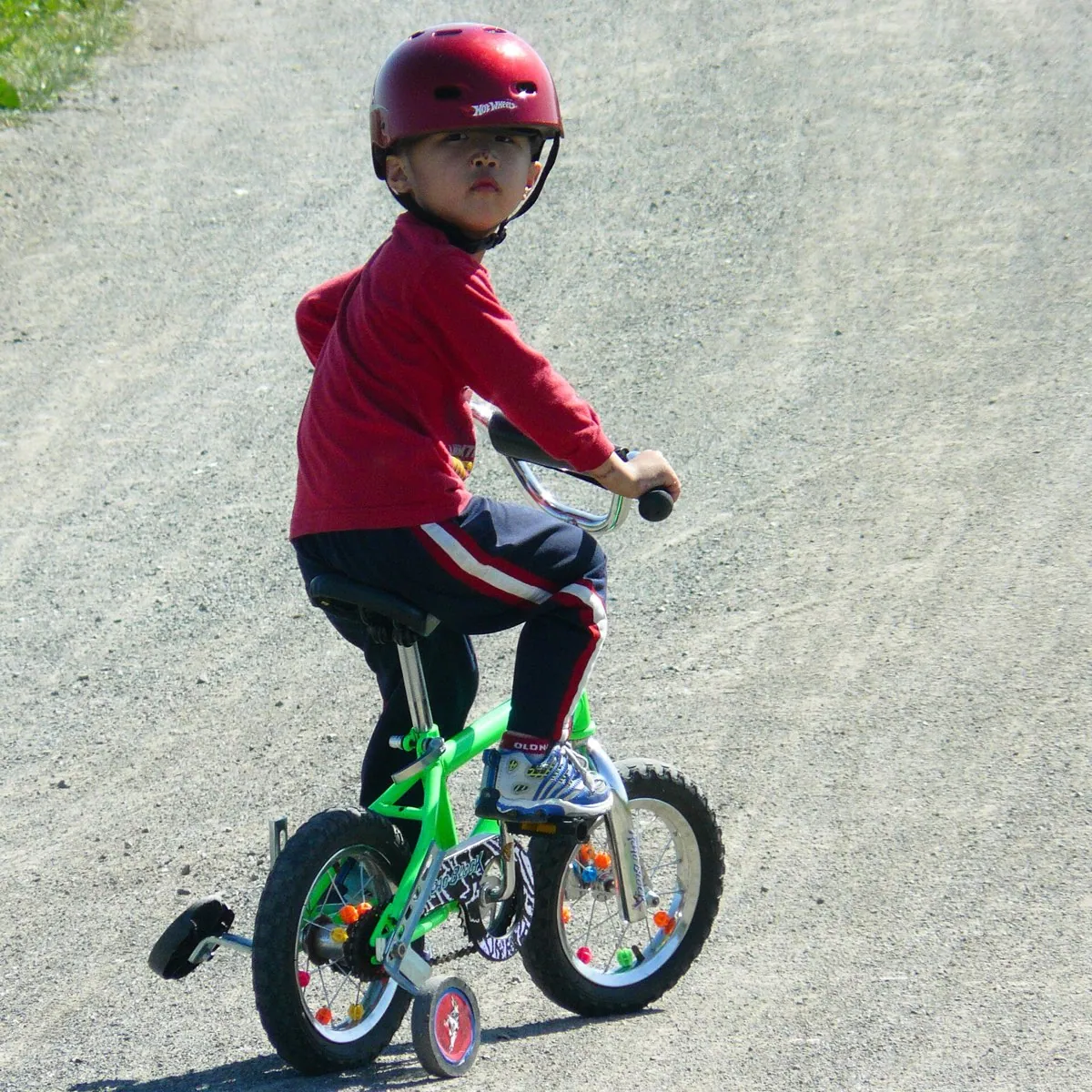 A helmeted boy riding a bicycle fitted with a pair of training wheels.